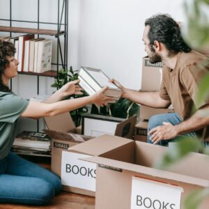 A couple organizing and packing books in cardboard boxes indoors, preparing for a move.