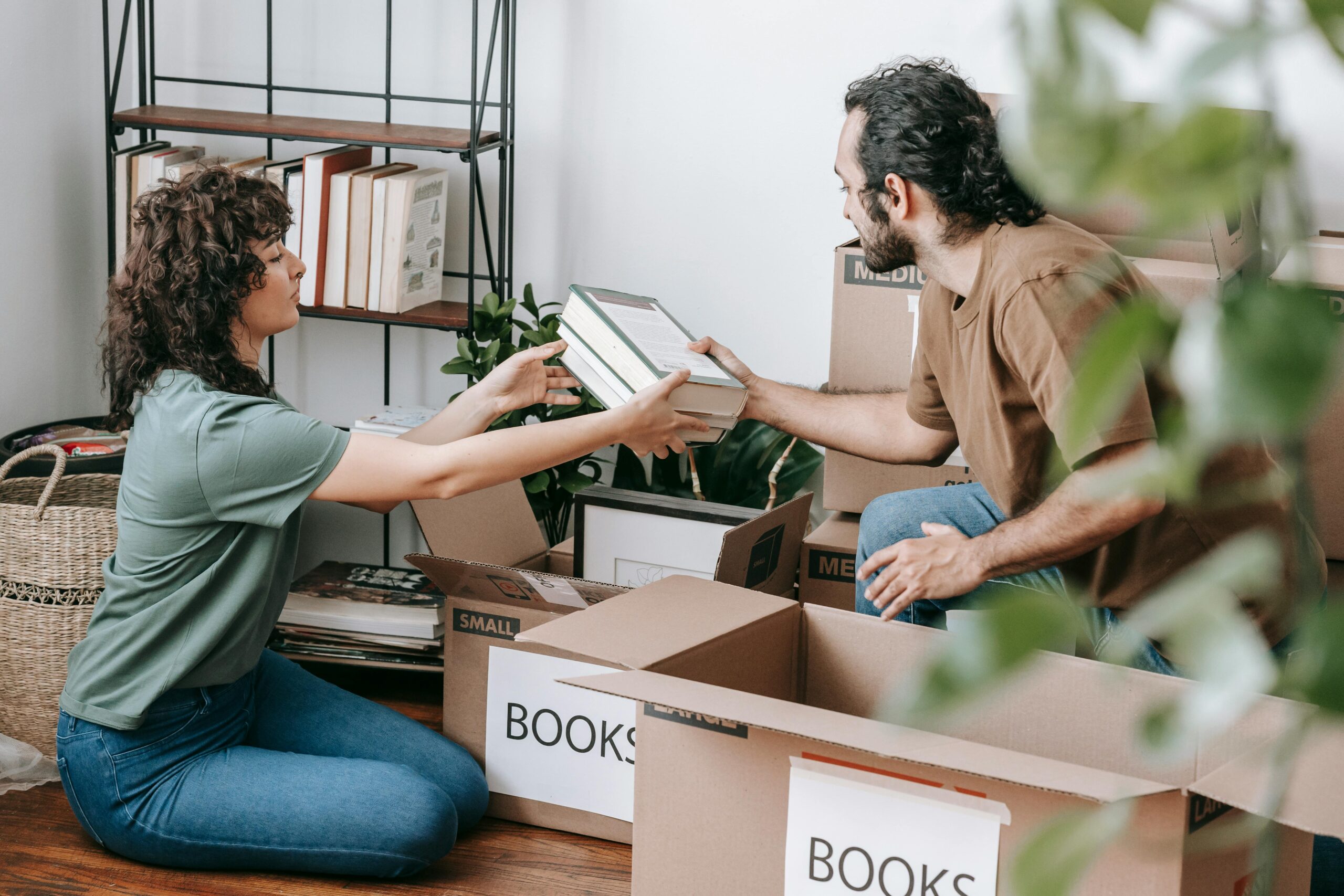 The Art of Letting Go: A Complete Guide to Decluttering Your Life 1 A couple organizing and packing books in cardboard boxes indoors, preparing for a move.