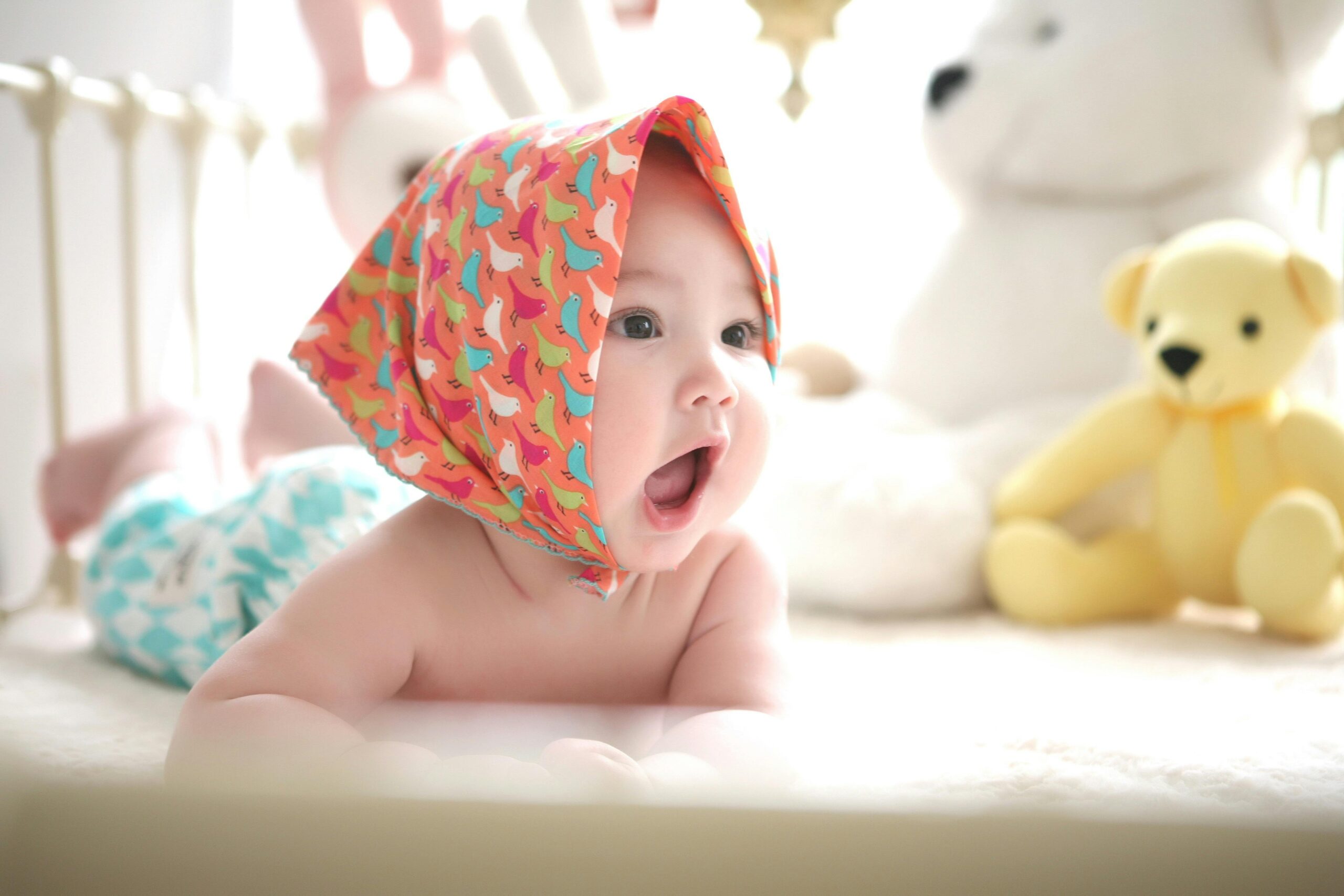 Baby Face Predictor – AI Baby Generator 4 Charming baby with colorful scarf surrounded by cute plush toys, highlighting innocence indoors.